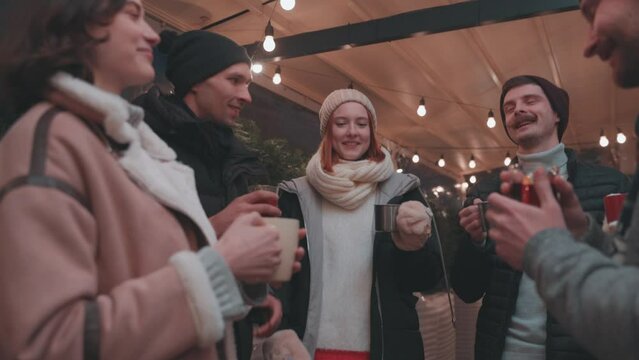 Party vibes. Happy smiling friends with cups of mulled wine having fun, spending time together at winter fair at evening time. Winter holidays