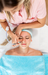 Beautician therapist applying face treatment in beauty salon to young woman.