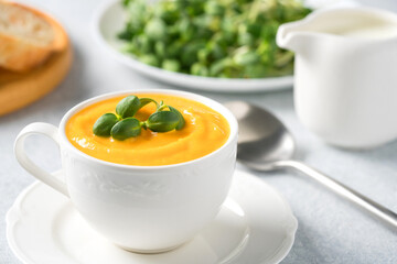 Cup of pumpkin cream soup garnished with fresh sunflower microgreen. Creamy butternut squash autumn soup in elegant white tea cup.  Front view, selective focus