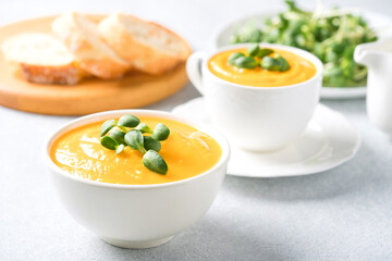 Bowl of butternut squash cream soup garnished with fresh sunflower microgreen. Creamy pumpkin fall soup in white bowls on the gray table. Front view, selective focus