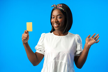 Young african woman holding credit card in hand against blue background