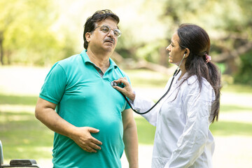Indian doctor check heartbeat of senior male patient outdoor at park. healthcare concept