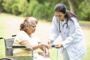 alzheimer. Indian doctor check pulse with oximeter device on finger of senior female diabetes patient in a wheelchair outdoor at park. Health care, Aging. Caregiver - Powered by Adobe