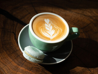 Cappuccino in big cup served with blue macaron on the wooden table.
