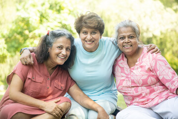 Happy Indian senior women having fun together outdoor - Elderly people hugging each other at summer park.
