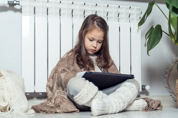 Serious, concentrated brunette girl use electronic tablet, play games, browsing in blanket, sit on floor near radiator - obrazy, fototapety, plakaty