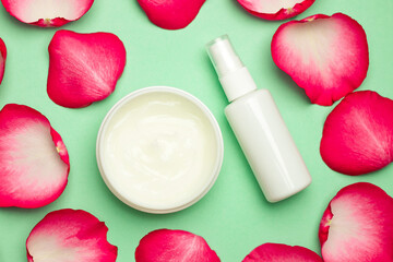 A jar of cream and lotion on a green background with rose petals. The concept of cosmetics.