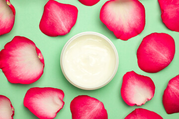 A jar of cream on a green background with rose petals. The concept of cosmetics.
