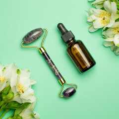 Face roller with beauty serum oil on a green background. Facial massage kit - for lifting massage, made of natural stones.