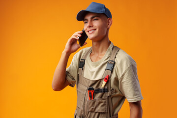 Young builder talking on a mobile phone against yellow background