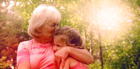 Fototapeta premium Loving cute granddaughter hugging her grandmother. Happy family. Having good times with grandparent outdoors. Love, connection, bonding concept