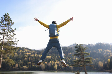 Happy man with open arms jumping, lake and mountains in background.