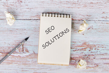 The text of SEO SOLUTIONS is written on a notebook sheet, business concept