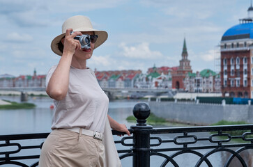 Woman tourist in a straw hat takes pictures on the street with a vintage camera