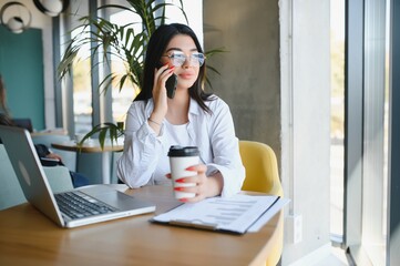Young charming female freelancer using laptop computer for distance job while sitting in modern coffee shop interior, beautiful Caucasian woman working on net-book during morning breakfast in cafe bar
