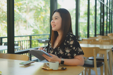 Female consultant is dreaming for work in the cafe with a cup of coffee while using tablet in coffee shop with relaxing moment. Female entrepreneur working in cafes.