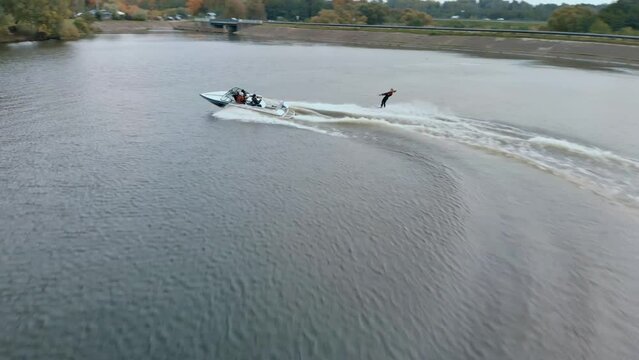 Drone Following Motor Boat Towing Wakeboarder on Scenic Lake in autumn. Aerial view (Side) of rider board behind speedboat on desert body of water. Wakeboarder performs water jumps and tricks