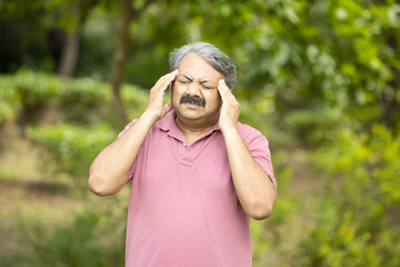Indian senior man suffering from headache standing outdoor at park. Stressed old people, - Powered by Adobe