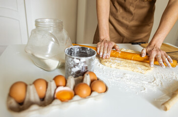 A woman in an apron prepares dough for baking at home. Rolling out and preparing dough for baking.