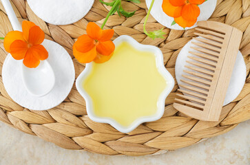 Small white bowl with cosmetic (massage, cleansing) aroma oil, wooden hairbrush, cotton pads and pansy flowers. Natural skin care, homemade spa and beauty treatment recipe. Top view.