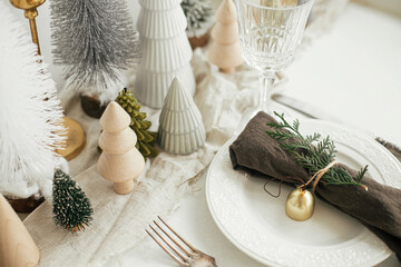 Christmas table setting. Stylish napkin with bell and fir on plate, vintage cutlery, glasses,...