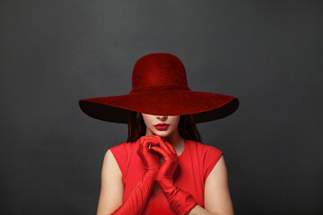 Stylish woman brunette with makeup and dark hair wearing red dress and red silk gloves and red wide broad brim hat on black background - obrazy, fototapety, plakaty