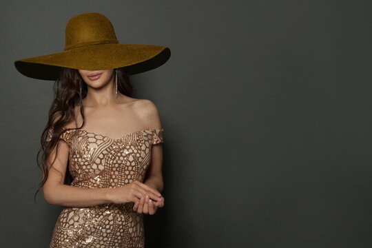 Cheerful fashionable woman fashion model wearing gold dress and brown broad brim hat smiling on black
