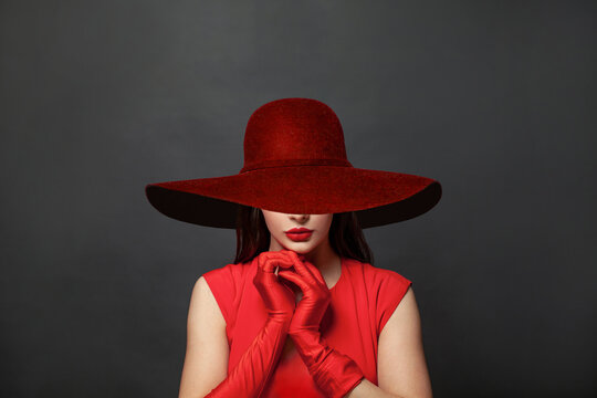 Stylish woman brunette with makeup and dark hair wearing red dress and red silk gloves and red wide broad brim hat on black background