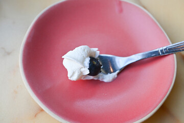 a bite of whipped cream with fresh blueberry with spoon on pastel plate selective focus