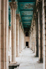 Colonnade of large baroque marble columns of an old noble hotel. The view leads down to a door. The...