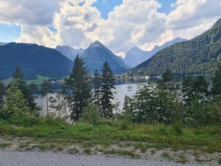 View from the shore of a lake surrounded by lush green mountain forests under blue cloudy sky