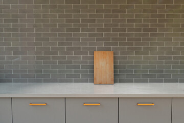 Focus on marble kitchen counter top. Grey tile background. Cutting board leaning.  Front view