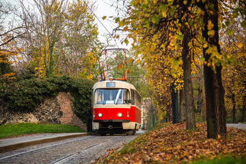 Naklejka na ściany i meble Old vintage tourist tram comes through the alley of a Prague city in an autumn day. Electric transport connection. Prague tram network is third largest in a world. Retro historic electro transport