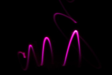 Curvas de luz de neòn color rosa en velocidad y desenfoque, con formas geomètricas en pico de ondas de mayor a menor,   forman un bello diseño abstracto en el espacio con fondo negro