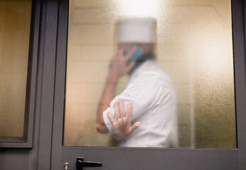 silhouette behind the glass of a man in a chef's uniform talking on the phone.