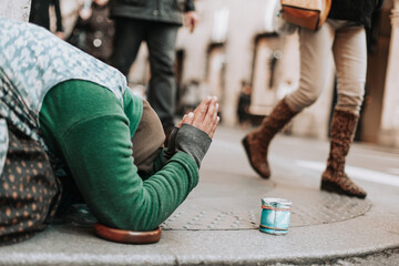a woman on her knees begs for alms on a city street. - obrazy, fototapety, plakaty