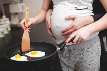 a pregnant girl and her husband are cooking scrambled eggs.
