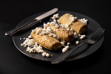pancakes with cheese on a plate and kitchen utensils on a black background