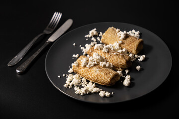 pancakes with cheese on a plate and kitchen utensils on a black background