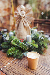 Coffee in eco friendly paper cup in winter garden with pine wreath