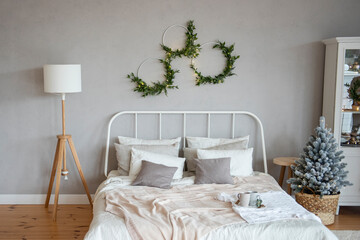 White wrought iron bed with textured milky throws and pillows on wood floor next to Christmas tree.