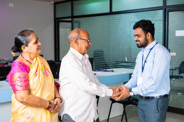 Happy smiling banker greeting by shaking hand of elderly couple at bank - concept of financial...