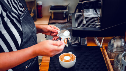 Hand of a barista in the coffee shop preparing to steam milk in the jug for a coffee cappuccino menu.