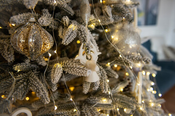Toys, garlands, balls with feathers, deer hang on artificial, snow-covered Christmas tree.