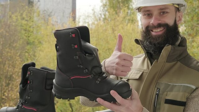 pair black Safety Shoes, work boots made of leather with reinforced cape, high top in hands of young bearded man, builder in uniform, concept of highest product quality, professional workwear