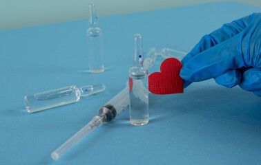 red heart in the doctor's hand. medicine ampoules and injection syringe.
