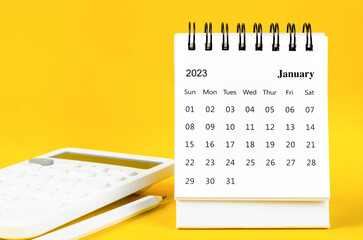 The January 2023 Monthly desk calendar for 2023 year and calculator with pen on yellow background.