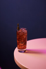 red cocktail with alcohol and ice and rosemary in a highball glass, on a white table