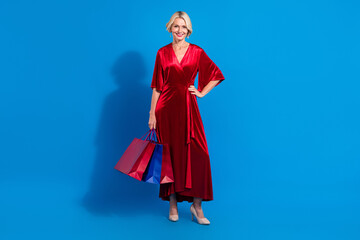 Obraz na płótnie Canvas Full length photo of charming cute senior lady wear red shiny dress holding bargains isolated blue color background