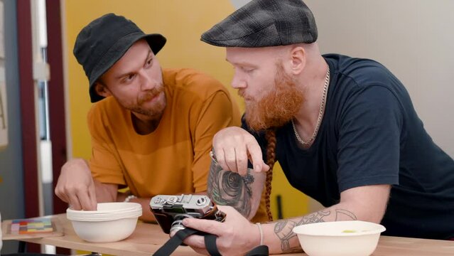 4K, Two male tourists who are best friends are standing at the counter in the hostel's living room. 2 men talking and eating snacks, another man holds a camera and opens a picture.